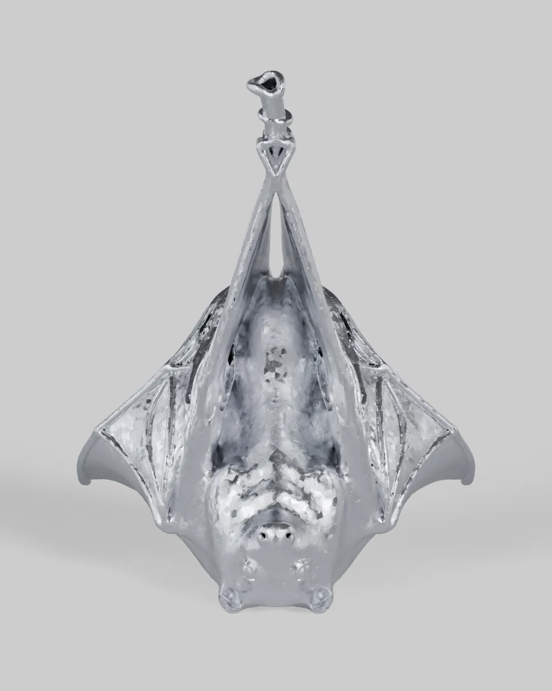 An aged, scratched-chrome bat with wings wrapped, hanging upside down.